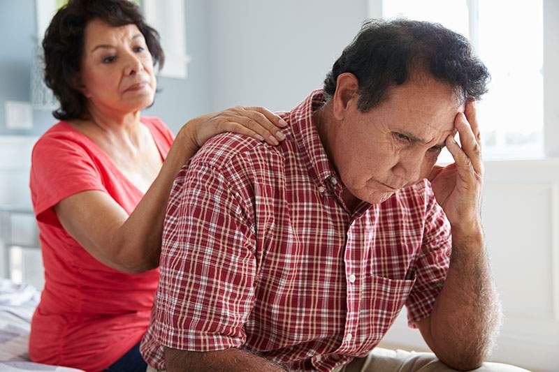 woman with hand on man's back who is holding his head